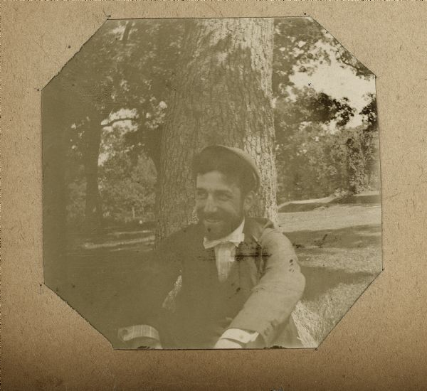 Portrait of a man sitting on the ground outdoors in front of a tree.