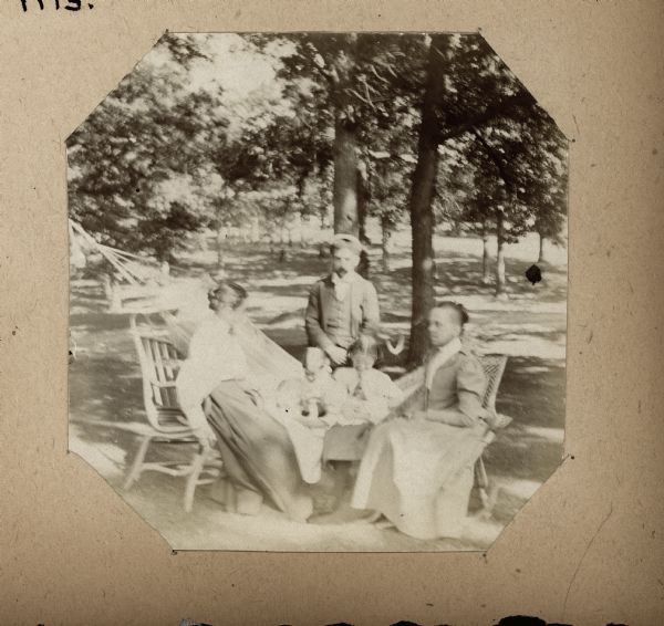 Outdoor group portrait of two women and one man are posing around two young children sitting in a hammock in yard.