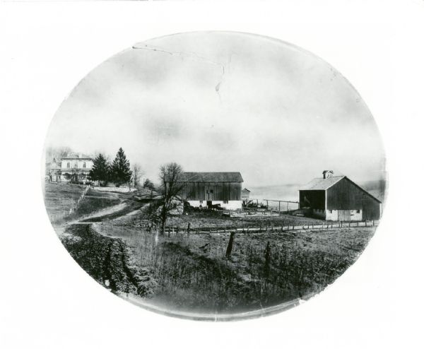 View towards a house and farm buildings. Caption reads: "Barneveld, Wis. Vic[inity]. Ridgeway Twp [township], Hwy [Highway] K. House built 1878 by William M. Jones. Jones was born in 1832 in Wales, came to America in 1840, and was at this farm in 1849. Loaned for copying through Steve Sennott, 1978, Elsa Greene, owner, 1988." From original hand-colored (?) photograph, oval shaped.