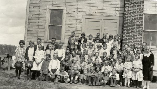 Group portrait of children and young adults posing outside a building. Caption reads: "A club of young Finlanders - Vilas Co. Every one has a field of potatoes. Good method of Americanization."