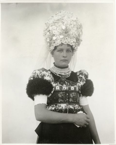 Three-quarter length portrait of a woman in traditional wedding costume. Caption reads: "Hungary - Mezokovesd. When the village beauty becomes a bride."