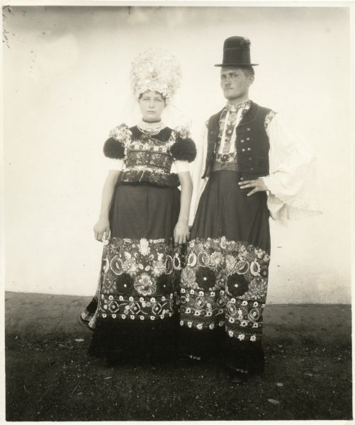 Full-length portrait of a woman and man standing and posing in traditional wedding costume. Caption reads: "HUNGARY. Mezokovesd (near Budapest), a bride and groom."