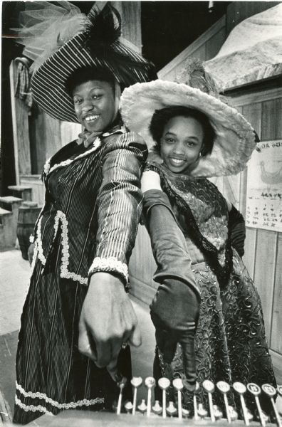 Two women in costumes posing and stretching out their arms towards the camera. Caption reads: "Phyllis Bickham (left) and Amber Kelly will alternate in the title role when North Division High School presents the musical 'Hello, Dolly' in opening its new theater. Proceeds from the performances - at 8 p.m. Friday and Saturday and April 6 and 7 and at 2 p.m. Sunday and April 8 - will go to the House of Peace Community Center, 1702 W. Walnut St. Directing the student cast are Arlene Skwierawski and Brother Booker T. Ashe."