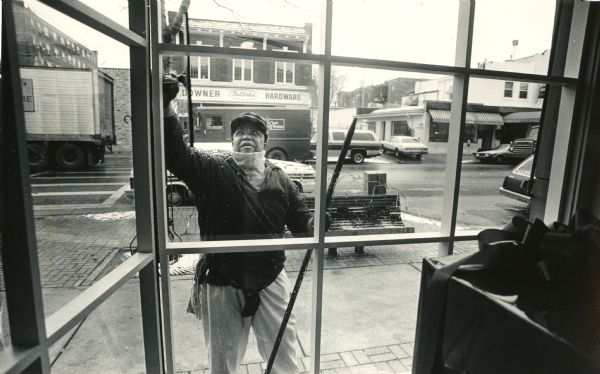 View looking out window at a man who is washing the window. Caption reads: "Edgar Gordon spreads cleanliness and happiness."  Edgar William Gordon was a window cleaner in Milwaukee, and he played alto horn in the First Brigade Civil War band. He made a lifelong mission out of encouraging positive interaction between white and black members of the community. He died in 1997.