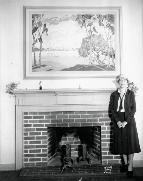Artist Jessie Kalmbach Chase standing near her painting above a fireplace at Lakewood School kindergarten room, 2314 Sherman Avenue. She is the only Madison woman listed in the "Who's Who of American Artists," published by the American Federation of Art.