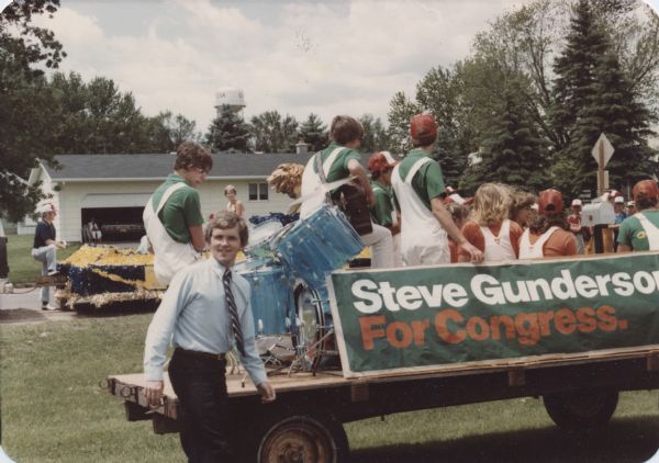 Steve Gunderson is standing next to a flatbed truck bearing a "Gunderson for Congress" banner. The truck is carrying a band and several supporters. Likely taken at a small town 4th of July parade.