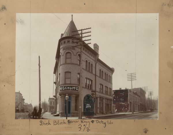 A Richardsonian Romanesque building built in 1889 by Christian W. Dick. The main window and door are blacked out, with the words "The Schlitz" hand written on the main window. The sign above the door is also hand written over the original photograph, reading: "The Schlitz." The entire side of the building behind the Christian Dick Block is blacked out. A note below the photograph reads: "Dick Block Corner King and Doty St. 3 1/2."