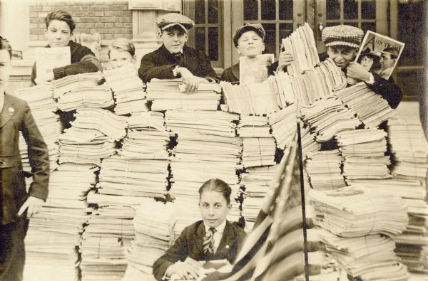 Several boys are posing with stacks of bound periodicals. An American flag is in the foreground. Caption reads: "Boys of Riverside High School, Milwaukee, with reading matter to send to the soldiers in France."