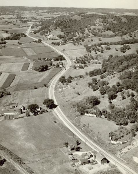 Aerial view of a road, with several farms, fields and hills along it. Caption reads: "U.S. 16 near La Crosse, Wis."