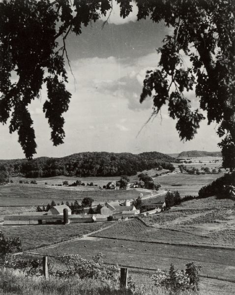 Elevated view of a large farm in a valley. Caption reads: "Prosperous Sauk County Dairy farm — nestling in a fertile valley between timber-clad hills. Photo: ca. 1945." 