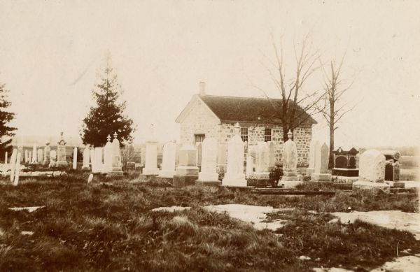 Exterior of a small church, with a cemetery in the foreground. Caption reads: "St. John's Evangelical Lutheran Church. Built 1864, Town of Dane, Dane County, Wisconsin. 34 x 22 ft., 12 ft. high. Used until a new church was built in the Town of Roxbury, 1905."