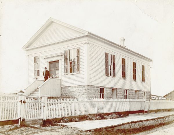 Exterior view of a church surrounded by a picket fence. A man is standing on the front steps. Caption reads: "Zoar Church, ca. 1890. Near Oshkosh Wis. and Wild Rose."