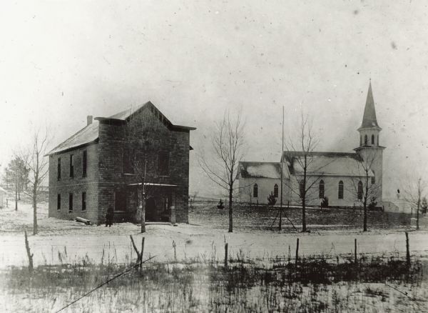 Exterior view of a church and a two-story building. Snow is on the ground and the trees are bare. Caption reads: "Pigeon Falls, Wis. 1913. Lutheran Church and Parish House. Copied from Lantern Slide, UW-BVI."
