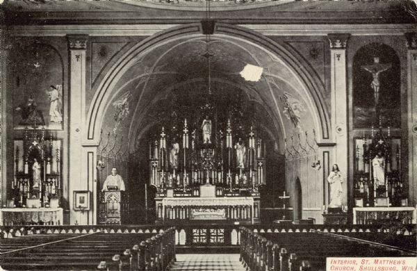Interior view looking towards the altar, nave, pulpit, and several statues. A priest is standing at the pulpit. Caption reads: "Interior, St. Matthews Church, Shullsberg, Wis."