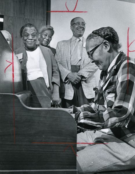 Several people are smiling and watching a woman playing a piano. Caption reads: "A HAPPY TUNE — Mrs. Earer Turner played spirituals and jazz for a group of residents from the Hillside Terrace housing project Friday when they visited the downtown YWCA for a morning of entertainment."