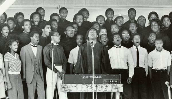 Members of a choir singing, with microphones in front of them. Caption reads: "Members of the Ebenezer Church of God in Christ performed a gospel drama Sunday at the State Fair."