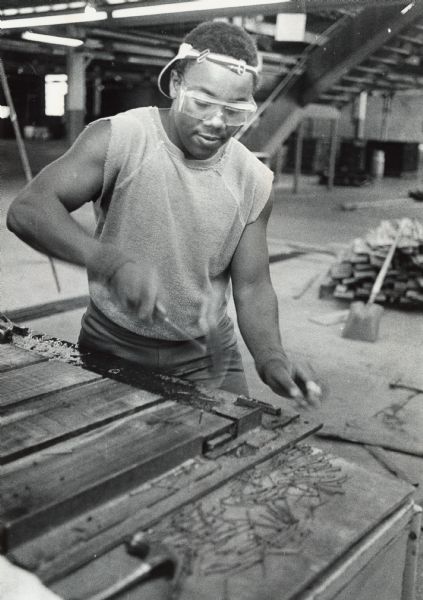 A young man is hammering a nail into a pallet. Caption reads: "Darnell Yarbrough, 18, worked on wooden pallets at the JA [Junior Achievement] workshop."