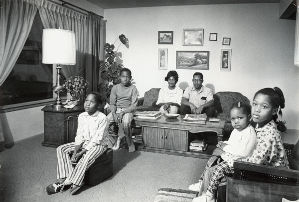 A family with four children sitting in their living room. Caption reads: "Mr. and Mrs. Boyzie Hughley, 8120 W. Beechwood Ave., sat in their living room with their children Janette, 7; Jeffrey, 11; Jennifer, 20 months, and Jan, 10. The Hughleys added carpeting and new furniture to their 235 home."