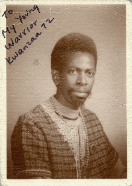 Waist-up portrait of Baba Hannibal Tirus Afrik, sent to an unnamed son for Kwanzaa 1972. Afrik was a school teacher and a leader in the creation of African culture-centered independent institutions in Chicago. In the year this photograph was taken, he had created Shule YA Watoto (school for children) on the west side of Chicago, which would be a self-sufficient school for more than 30 years. On the photograph's front, Afrik has written: "To My Young Warrior, Kwanzaa 72." On the back he has written" "'If I return I shall kiss you, But if I fall, I shall ask you to do as I have done in the name of REVOLUTION.' Your Warrior Father, Hannibal Tirus Afrik. UMOJA 12-26-72."
The quotation is the title given to a book Emory Douglas wrote for the Black Panther Party, and was there claimed as an old Cuban proverb.