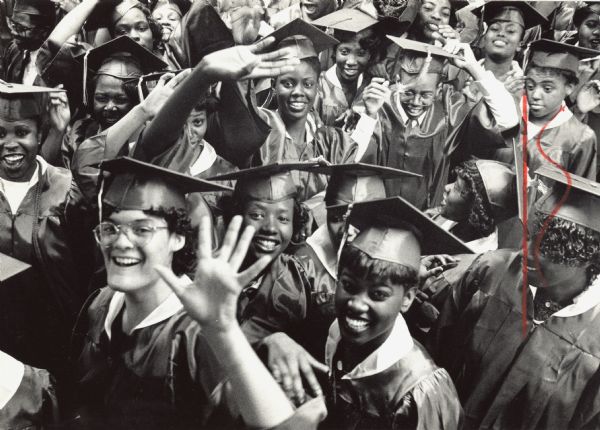 Elevated view of high school students in caps and gowns smiling and waving. Caption reads: "North Division seniors kidded around as they prepared to march into the auditorium during Senior Day."