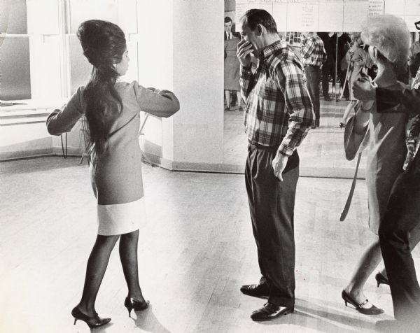 A woman demonstrating a dance move while a man is watching. Caption reads: "Concentration is required when taking a dance lesson. Miss Maria Diaz, an instructor at a downtown dance studio, showed Don Dahms, 2172 S. 6th St., a step in one of the new dances. Instructors also teach older dances."