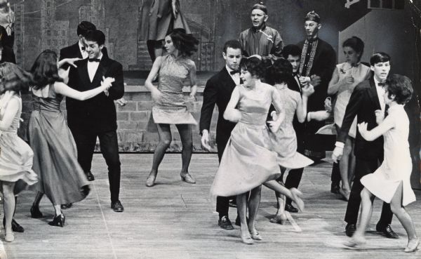 Several actors, all of whom are white and are wearing "yellowface" makeup to caricature Asians, are either dancing or looking on. Caption reads: "The Chinese elders looked on in horror as their Americanized offspring danced in a most unoriental manner. This was one of the production numbers in 'Flower Drum Song,' the Rodgers and Hammerstein musical that opened Wednesday night at the Sunset Playhouse in Elm Grove."