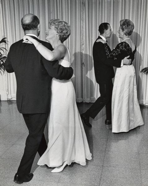 Two couples are dancing in a ballroom with full-length curtains in the background. Caption reads: "The dance music appealed to (from left) Mr. and Mrs. Joseph Sampson, 2108 E. Edgewood Av., Shorewood, and Carl Muenzner, 743 N. 25th St., and Miss Margaret Millmann, 3939 N. Murray Av., Shorwood. Grant Krueger and his orchestra played."