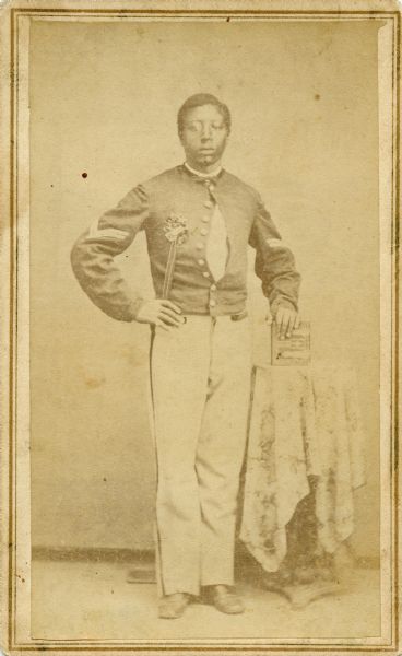 Carte-de-visite full length portrait of a young soldier posing next to a table. His hand is resting on what appears to be a book. The reverse of the card identifies him as Thomas Nowell, of the 54[th] U.S.C.T. [United States Colored Troops] Co. T. The caption reads: "A pupil of my mother's in the schools for the freedmen established in South [<i>sic</i>] by the American Missionary Association after the Civil War."

The mother mentioned in the caption is Katherine Schloesser Estabrook.