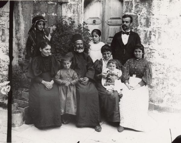 Nine children and adults posing for a group portrait outdoors. Caption reads: "Syrians. Protestant group."