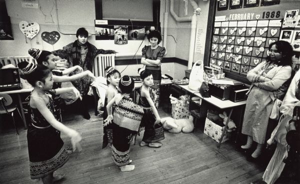 Five students in costume are dancing while several adults are looking on. Caption reads: "SHALL WE DANCE? Children practiced an Asian dance before performing in the Heritage Night program this week at 38th Street School. Heritage Night highlighted the ethnic backgrounds of the children attending the school."
