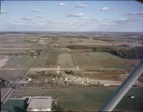 Aerial view of rural landscape with suburban construction in foreground. Cottage Grove Road is at left with the newly constructed Acewood Boulevard crossing near the center. Homes are under construction on Vernon Avenue. A sign in a field at right advertises for Acewood Homes. Central Storage & Warehouse (currently Y Not Foods)4309 Cottage Grove Rd., can be seen at lower left and Good Shepard Methodist Church, 602 Acewood Blvd., is also visible. Several farms dot the landscape in the distance.