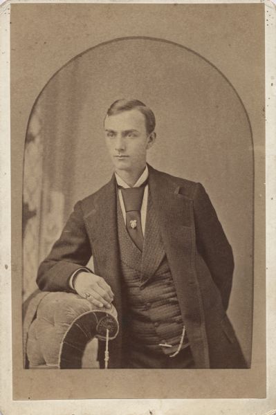 Waist-up studio portrait of Publius V. Lawson, of Menasha, standing and leaning against a chair. Portrait was taken when he was a senior at the University of Wisconsin.