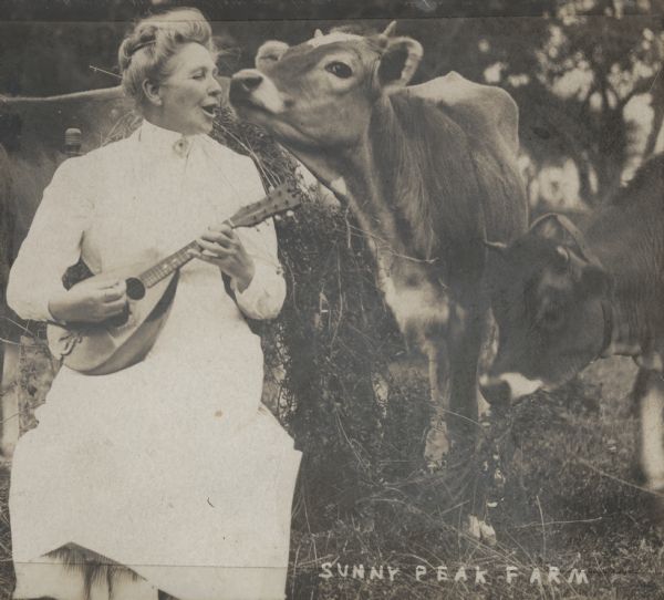 Adda Howie, sitting outdoors in a chair, playing a mandolin and singing for her dairy cows at Sunny Peak Farm.