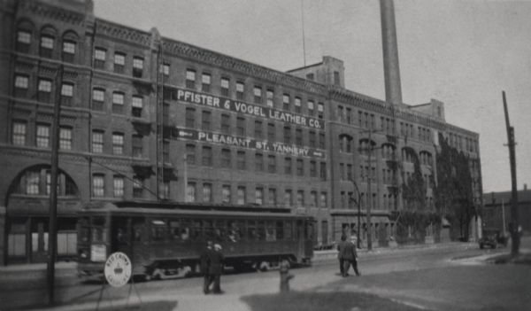 Exterior view of the Pfister and Vogel Tannery at 1531 North Water Street. A streetcar, a Red Crown Gasoline sign and pedestrians are in the foreground.