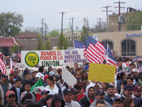 Elevated view of a large group of people, largely from the Latino community, marching from Walker's Point, through the downtown, to the Lake Michigan lakefront. Many people are carrying signs and U.S. flags. The march was organized to protest restrictive U.S. immigration laws. 