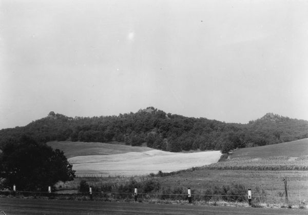 View across road and fields towards three wooded hill peaks. A roadside fence is in the foreground. Caption reads: "D.A. 36-268 — Three peaks on Hy.71 between Sparta and Norwalk."