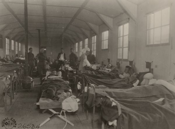 Lieutenant Harry Humphreys, A.R.C. entertaining wounded men in Ward K of American Evacuation Hospital #114, Fleury-sur-Aire, France. Miss Grace Van Wormer, A.R.C., at center, is in charge of the ward.