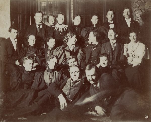 Group portrait of twenty men and women, posing casually, but wearing suits and dresses. The image reverse identifies them as members of the Up-To-Date Club.