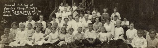 Group portrait of twenty-one women and twenty-four children, posing on and in front of the wooden steps of a building. The caption identifies the group as No. 88 of the Eureka Hive of the Lady Maccabees, which was a fraternal organization that provided low-cost insurance to members.