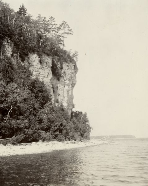 View across water towards a cliff face overlooking a beach and Lake Michigan.