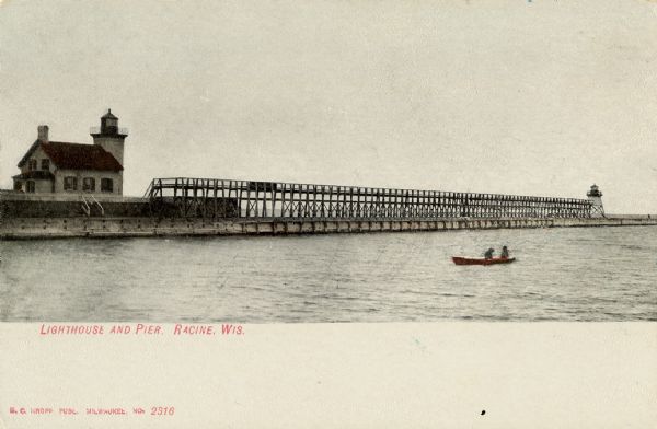 Tinted postcard of the lighthouse and a light tower at the end of a pier. A small boat with two passengers is on the water. This would be the Racine North Breakwater Lighthouse, and the Racine North Pierhead Light. Around 1916, the pierhead tower was moved and replaced with a post light.
