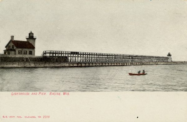 Tinted postcard of the lighthouse and a light tower at the end of a pier. A small boat with two passengers is on the water. This would be the Racine North Breakwater Lighthouse, and the Racine North Pierhead Light. Around 1916, the pierhead tower was moved and replaced with a post light. Caption reads: "Lighthouse and Pier, Racine, Wis."