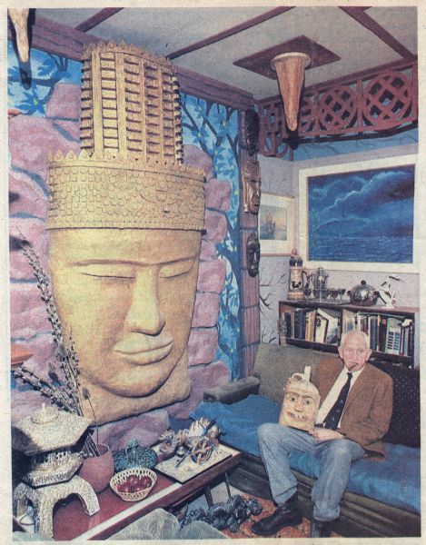 View of Sid Boyum sitting in his living room at 237 Waubesa Street. He is sitting on a couch and holding a jug previously used for vinegar, which he sculpted into a face using wood and sawdust.