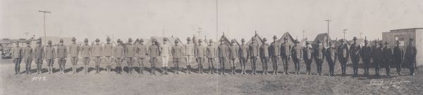 A panoramic group portrait of the officers of the 6th Battalion at Camp MacArthur. An automobile in the background on the left has a sign painted on the windshield that reads: "Stats & Simpson, Authorized Camp Photographer, Phone 989."