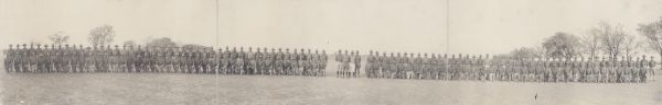 A panoramic group photograph of military units at Camp MacArthur. In the background are trees and buildings.