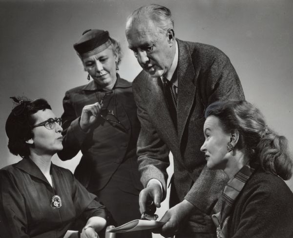 A man is showing a folded sheet of paper to three women and is gesturing toward it with his pipe. Caption reads: "An educational expert, Dr. Carleton Washburne, director of graduate studies and teacher education at Brooklyn (N.Y.) college, was brought to Underwood school, 11132 W. Potter Rd., Wauwatosa, Wednesday for a speaking engagement by a group of mothers. He is shown with (from left) Mrs. Leon Hamlet, 2517 N. 100th St.; Mrs. Carlin Turner, 11602 W. Potter Rd., and Mrs. Martin Kuban, 7343 Milwaukee Av.
