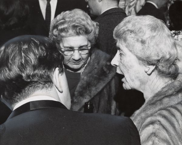 A woman in the foreground on the right is speaking to a man and another woman; the top of an opened bottle of champagne is between the group. Caption reads: "Miss Paula Uihlein (right), 3319 N. Lake Dr., drank champagne with guests at a party following the Saturday night opening of 'The Marriage of Figaro' at the Skylight on the Square. With her were Mrs. Clinton E. Stryker, 7030 N. Barnett Lane, Fox Point, and producer Clair Richardson."