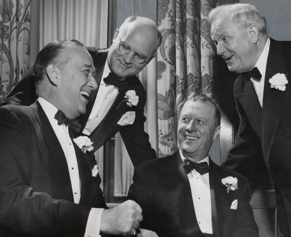 Four men in tuxedos smiling and talking to each other. Drapes are in the background. Caption reads: "Among others at the dinner were (from left) W.W. Brown, Chicago, president of the Chicago, Indianapolis and Louisville Railroad; A.S. Genet, Chicago, vice-president of the Chesapeake & Ohio Railroad; Paul Feucht, Chicago, president of the North Western Road, and W.A. Roberts, president of Allis-Chalmers Manufacturing Co."