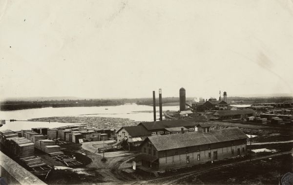 Elevated view of a lumber plant, with large stacks of lumber stacked around it. A lake is behind the plant.