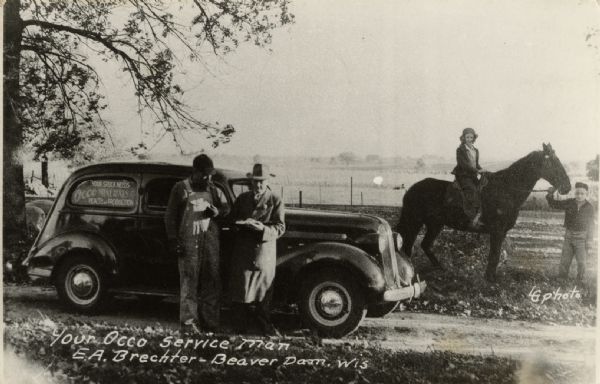 A man in an overcoat is leaning against a parked car, with a man in overalls standing next to him. A sign in the car window reads: "Your stock needs Occo Minerals for health and production." Behind the car, a woman is sitting on a horse, and a young man or boy is holding the reins of the horse. Caption reads: "Your Occo Service Man, E.A. Brechter — Beaver Dam, Wis."
The postcard is addressed to Mr. M. Kledehn of Burnett, and the message reads: "Mr. Kledehn, If you have any abortion mastitis or breeding trouble in your herd, we can correct it for you. All services (are free) Phone 1168W. We also treat pigs for necro & spray them for mange. A trial will convince you. Mr. Brechter."